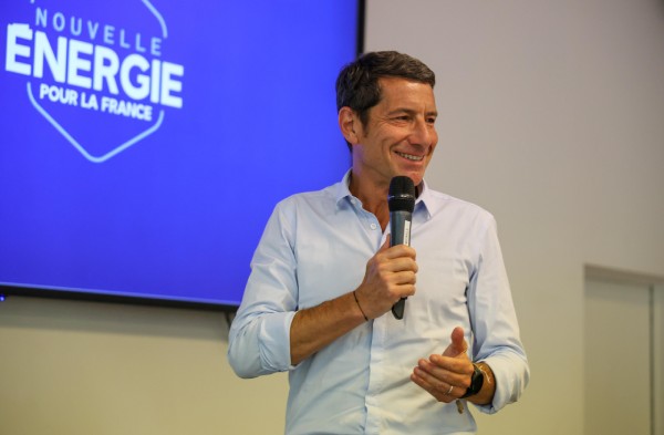 David Lisnard, en chemise et micro à la main, donnant un discours devant un panneau Nouvelle Énergie pour la France