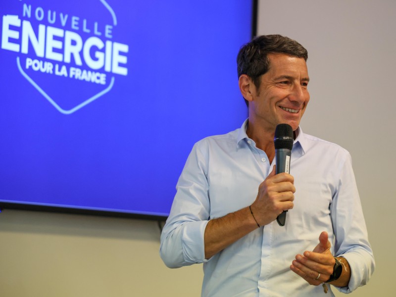David Lisnard, en chemise et micro à la main, donnant un discours devant un panneau Nouvelle Énergie pour la France